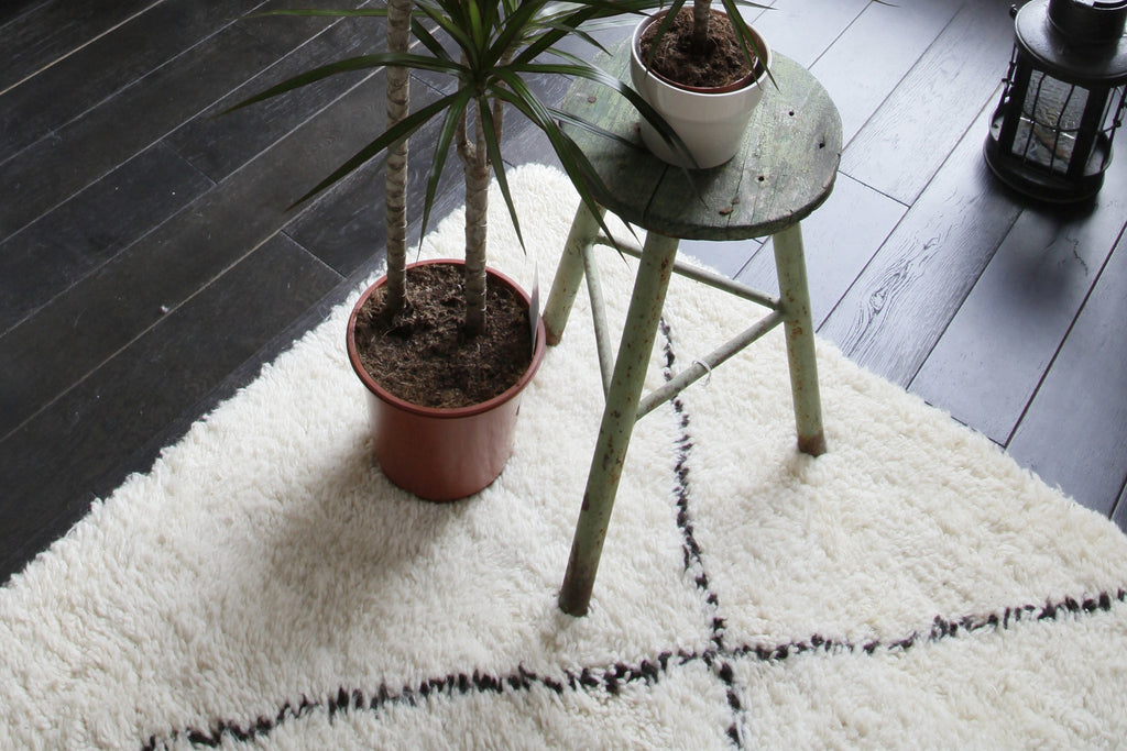 Close-up of corner of woollen hand-knotted Beni Ouarain rug, with plant pot and stool.