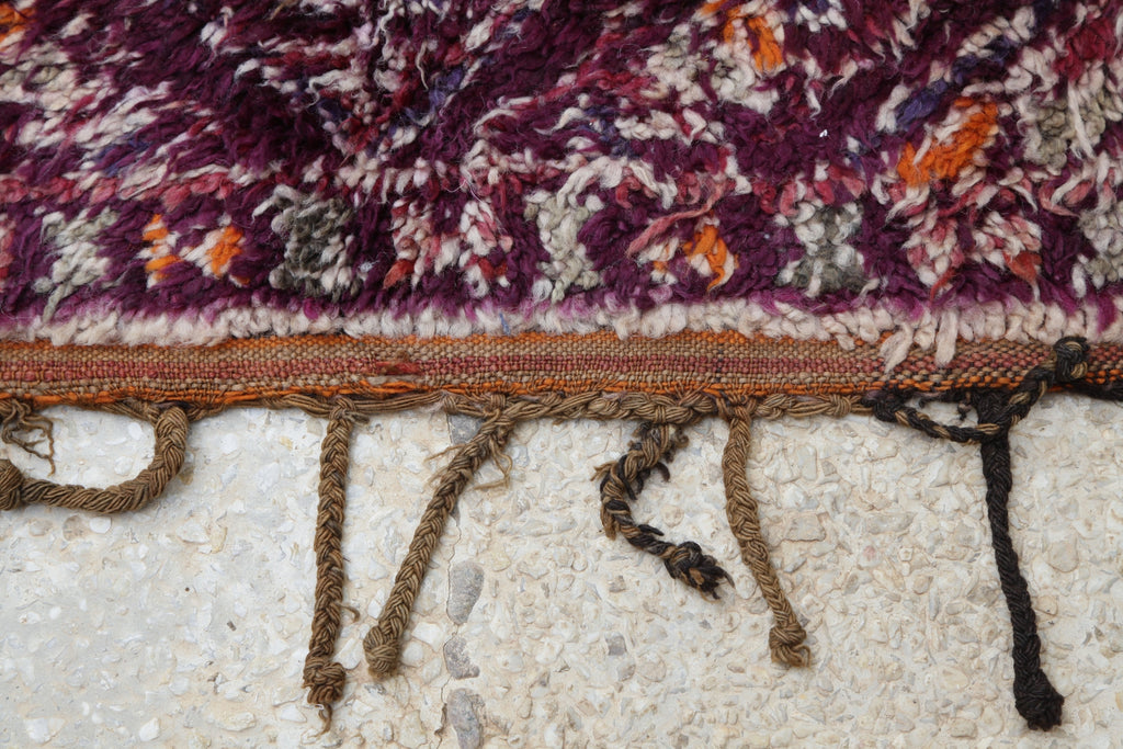 Close-up of the end of the beautiful Beni M'Guild Moroccan Berber rug, showing a narrow flat-weave section and long brown and black tassels.